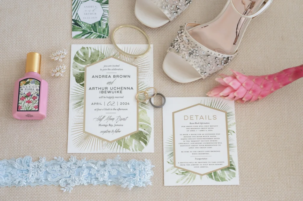 Arthur-Andrea-Jamaica-Halfmoon-Wedding-140.jpg - OMOS Photography Wedding invitations and details spread on a beige fabric, with a pink Gucci Flora perfume bottle, jeweled sandals, bracelets, and lace trim nearby