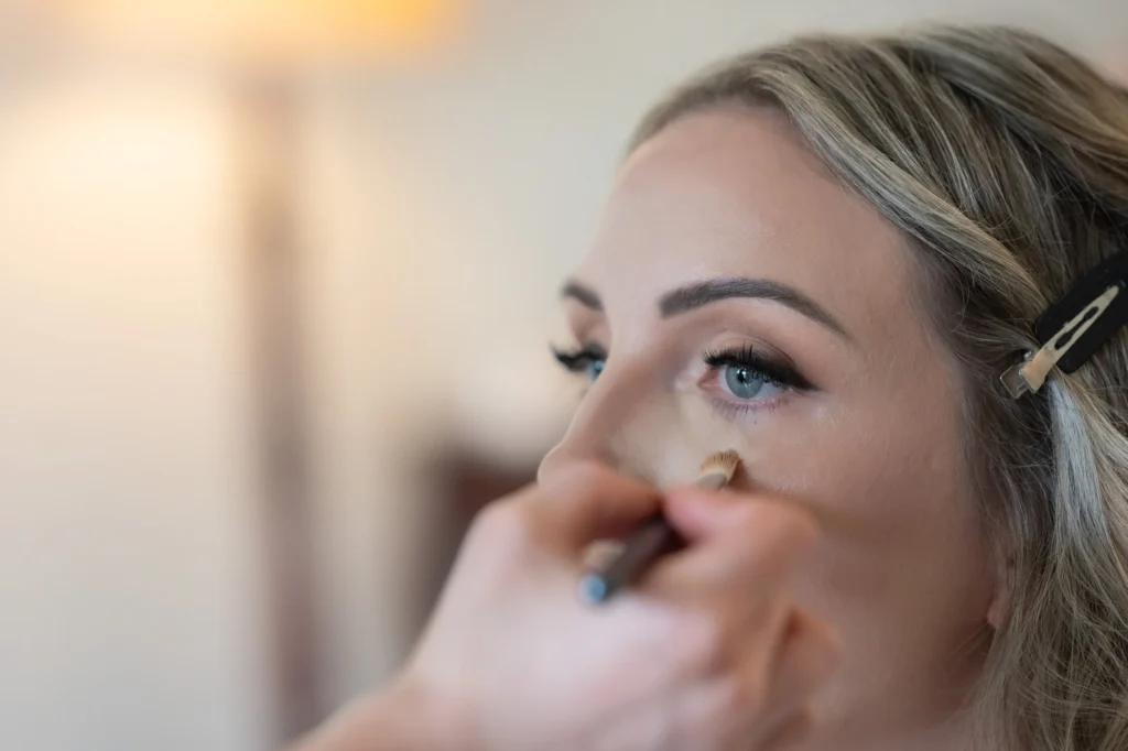Arthur-Andrea-Jamaica-Halfmoon-Wedding-147.jpg - OMOS Photography Close-up of a person applying makeup under the eye with a brush, hair clipped back with a clip nearby.