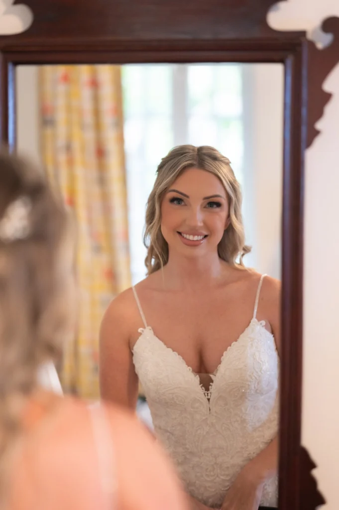 Arthur-Andrea-Jamaica-Halfmoon-Wedding-174.jpg - OMOS Photography Bride in a white lace wedding gown smiles at her reflection in a wooden-framed mirror.