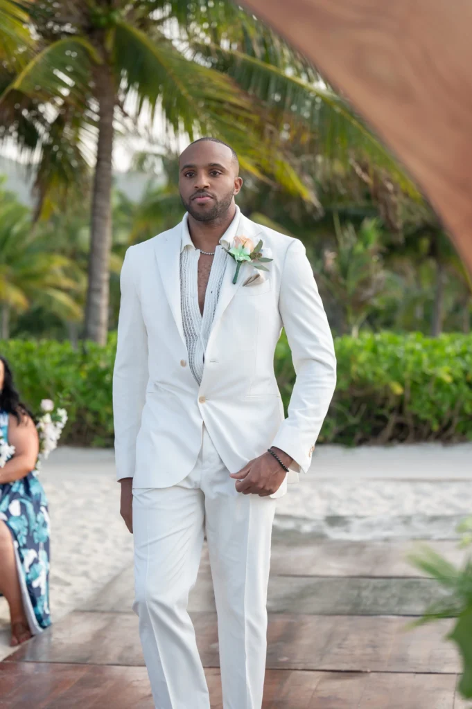 Arthur-Andrea-Jamaica-Halfmoon-Wedding-226.jpg - OMOS Photography Man in a light white suit standing on a wooden deck at a tropical beach, boutonniere on the lapel.