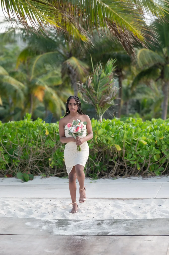 Arthur-Andrea-Jamaica-Halfmoon-Wedding-232.jpg - OMOS Photography Bride in a strapless beige dress holding a pink and white bouquet while standing on a sandy beach with lush tropical greenery in the background.