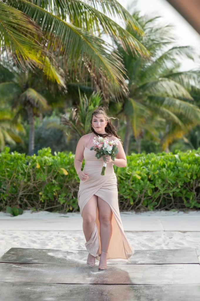 Arthur-Andrea-Jamaica-Halfmoon-Wedding-238.jpg - OMOS Photography Woman in a beige gown walking on a beach boardwalk, holding a bouquet with tropical palm trees in the background