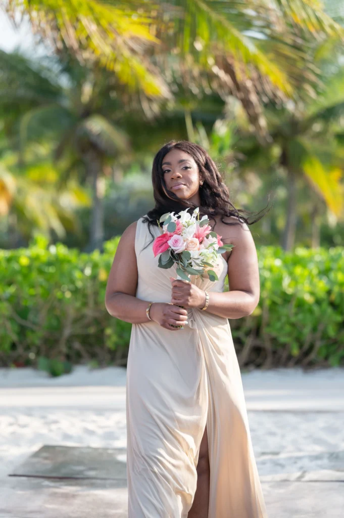 Arthur-Andrea-Jamaica-Halfmoon-Wedding-241.jpg - OMOS Photography Woman in a beige dress on a sunny beach holding a pink and white bouquet.