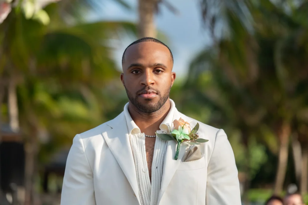 Arthur-Andrea-Jamaica-Halfmoon-Wedding-243.jpg - OMOS Photography Close-up portrait of a man in a light suit with a boutonniere at an outdoor event.