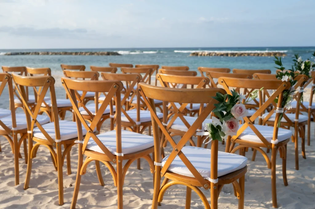 Arthur-Andrea-Jamaica-Halfmoon-Wedding-316.jpg - OMOS Photography Rows of wooden folding chairs with white cushions on the sandy beach, facing the ocean, decorated with pink and white flowers on the ends of the rows.