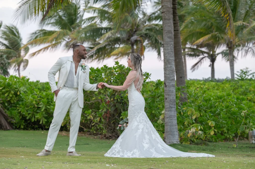 Arthur-Andrea-Jamaica-Halfmoon-Wedding-420.jpg - OMOS Photography Bride in a lace wedding gown and groom in a light suit hold hands in a tropical garden setting.