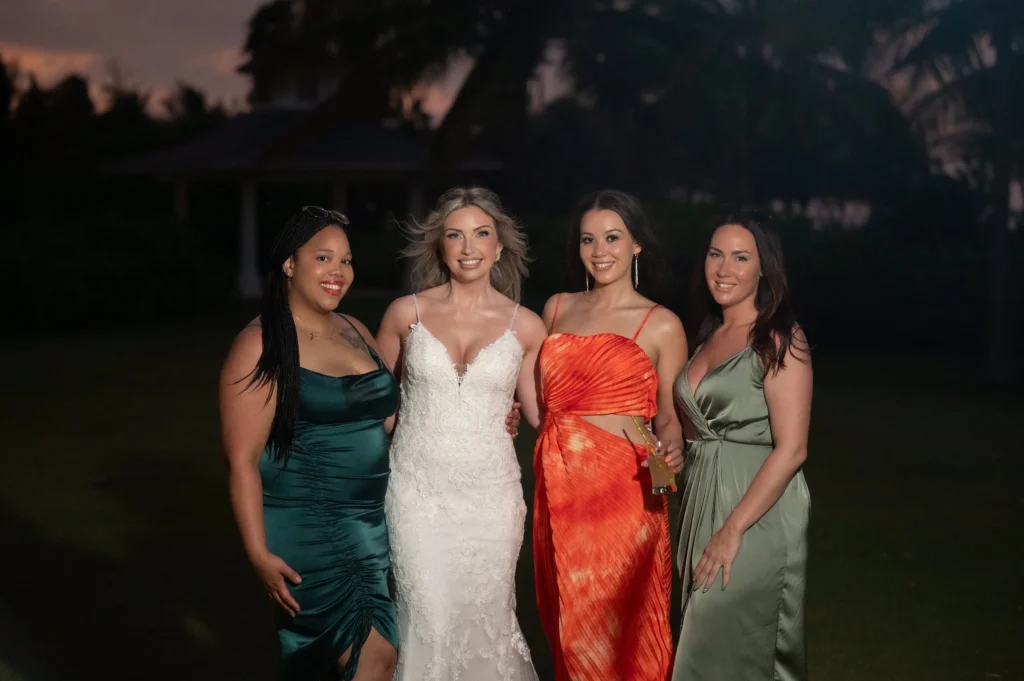 Arthur-Andrea-Jamaica-Halfmoon-Wedding-441.jpg - OMOS Photography Four women posing outdoors at dusk, one in a white lace dress and the others in teal, orange, and sage green gowns, smiling for the photo.