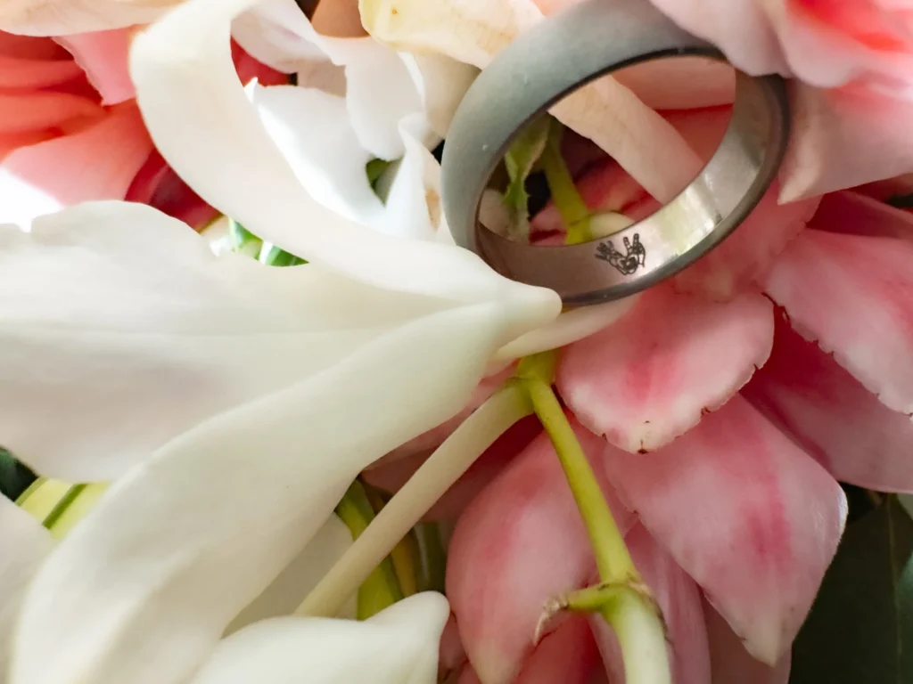 Arthur-Andrea-Jamaica-Halfmoon-Wedding-525.jpg - OMOS Photography Close-up of a silver ring nestled among pink and white flower petals, partially reflecting light.