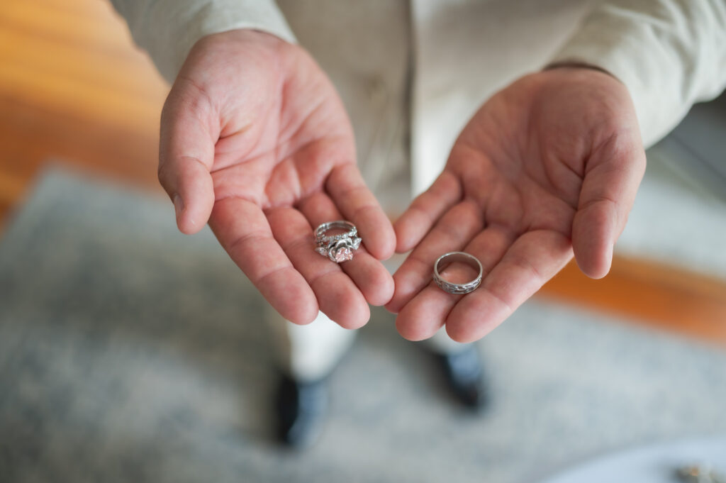 Close-up of hands cupped together holding three silver rings, including a detailed engagement-style ring, against a blurred background.