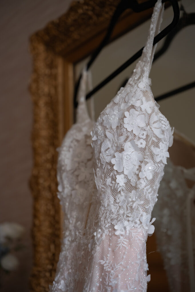 Close-up of a white lace wedding dress with 3D floral appliqués on a black hanger