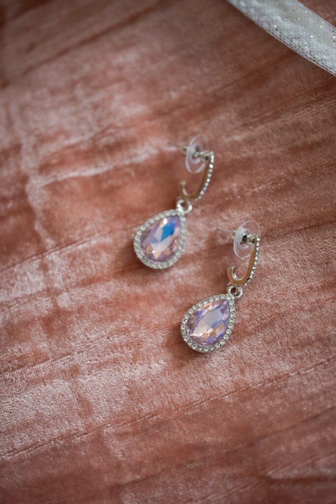 Silver bracelet with pink teardrop gemstones surrounded by a halo of small clear stones on pink velvet fabric.