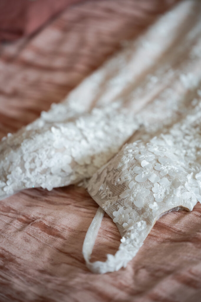 Close-up of white lace with floral appliques on pink satin fabric (wedding-dress detail).